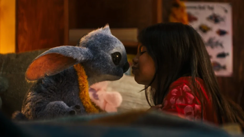 Lilo leaning in to kiss Stitch in Disney's live-action Lilo & Stitch movie, showing their heartwarming bond in a cozy indoor setting