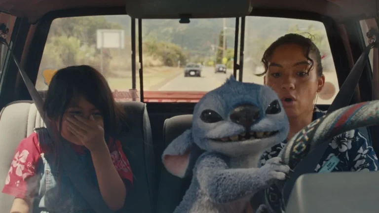 Stitch playfully grabs the steering wheel while riding in a car with Lilo and Nani in Disney’s live-action Lilo & Stitch movie.