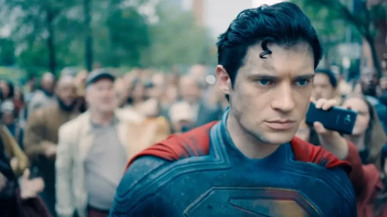 David Corenswet as Superman in a gritty costume, with a curl of hair and dirt on his face, looking determinedly forward amidst a blurry crowd.